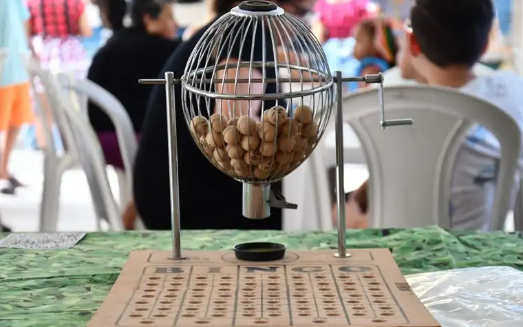 metal wire bingo cage holding numbered wooden balls on a stand above a wooden board with numbered holes, set on a green cloth