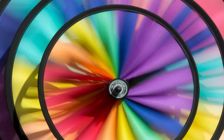 motion-blurred spinning wheel with rainbow-colored spokes in red, orange, yellow, green, blue and purple inside a black circular frame