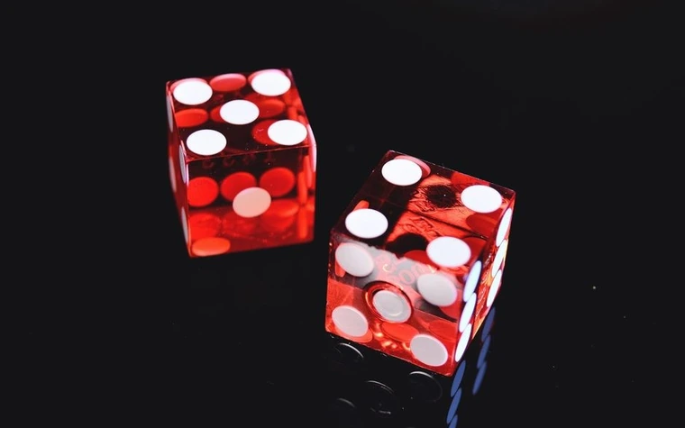 two translucent red dice with white pips resting on a black reflective surface against a dark background