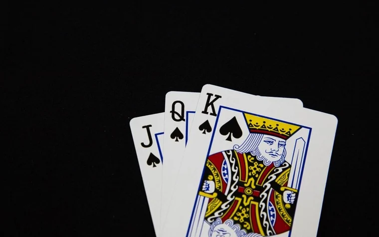 jack, queen and king of spades playing cards fanned on a plain black background
