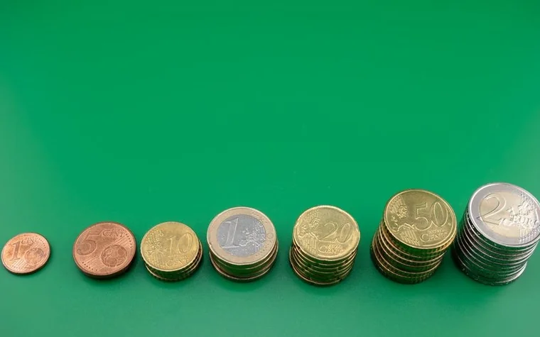 seven stacks of euro coins in rising order from one cent to two euros on a flat green background, each stack taller than the last