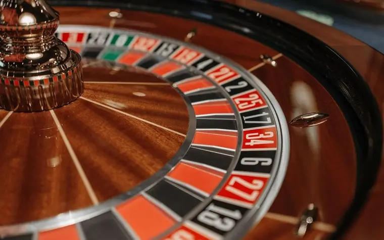 close-up of a roulette wheel with a brass spindle at the centre and red and black numbered pockets set in a polished wooden bowl