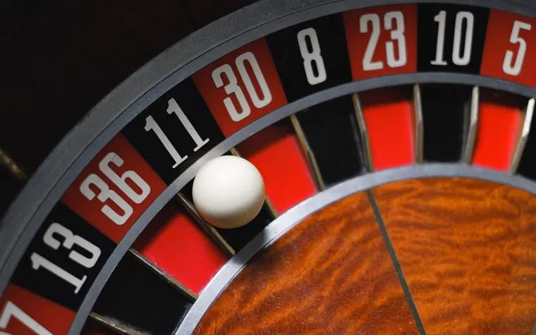 white roulette ball resting in a pocket of a wheel with red and black numbered slots beside a wooden central cone