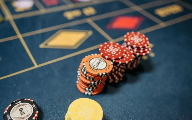 stacks of red and orange casino chips with a single yellow chip on a blue roulette layout marked with gold diamond shapes