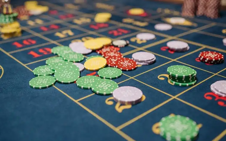 Green, red, yellow, and white casino chips scattered and stacked on a blue felt roulette table