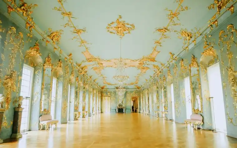 Ornate baroque hall with gold ceiling detail and rows of tall arched windows