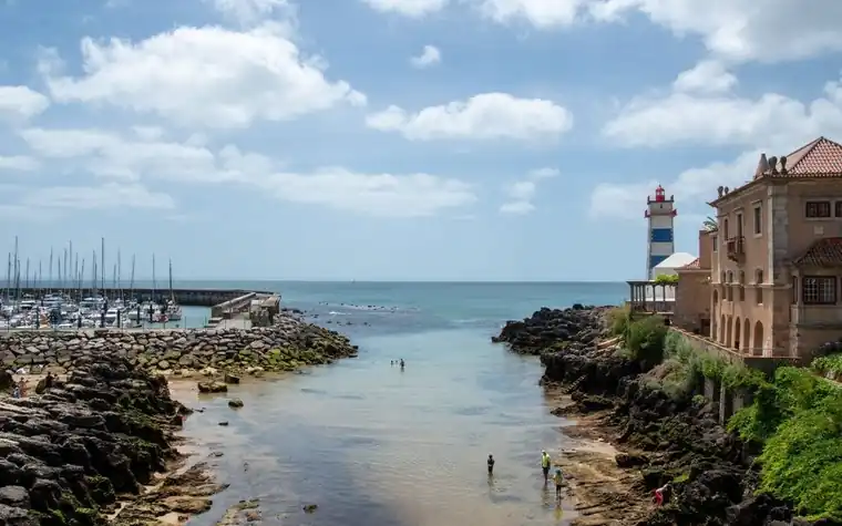 Small rocky inlet with a white lighthouse tower and a marina in the distance on a sunny day