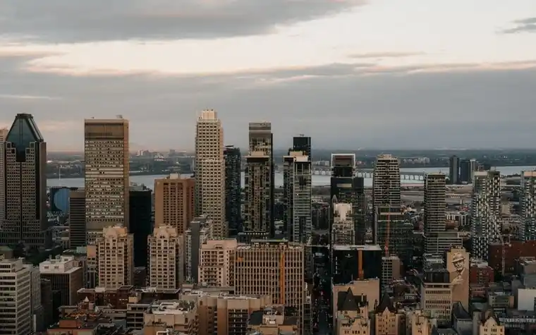 Downtown skyscrapers of a large city at dusk with a wide river and distant horizon behind them