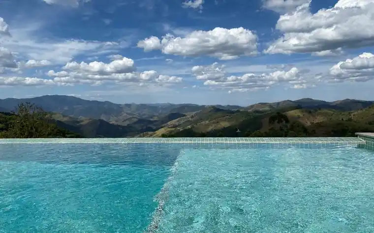 Bright turquoise infinity pool with the edge disappearing into a mountain range under a partly cloudy sky