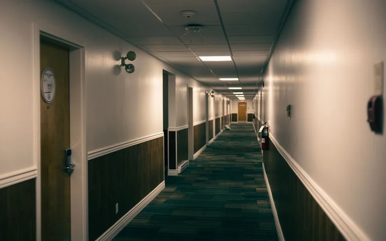 long hotel corridor with closed wooden doors and dim ceiling lights receding into the distance