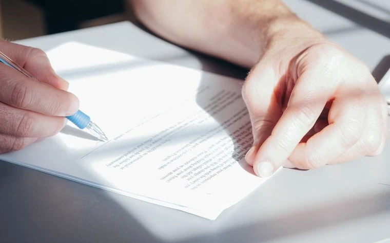 close-up of a hand holding a fountain pen poised over a paper document ready to sign