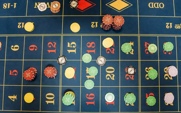 overhead view of a roulette table layout covered in stacked casino chips of different colors scattered across the numbers