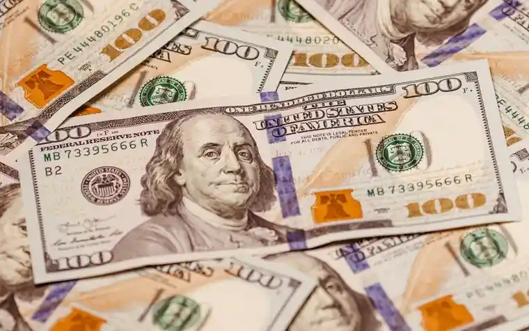 close-up of scattered hundred dollar bills overlapping each other on a flat surface