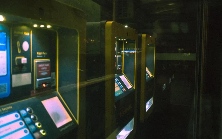 row of illuminated self-service ticket machines with glowing screens and bill slots in a dim room