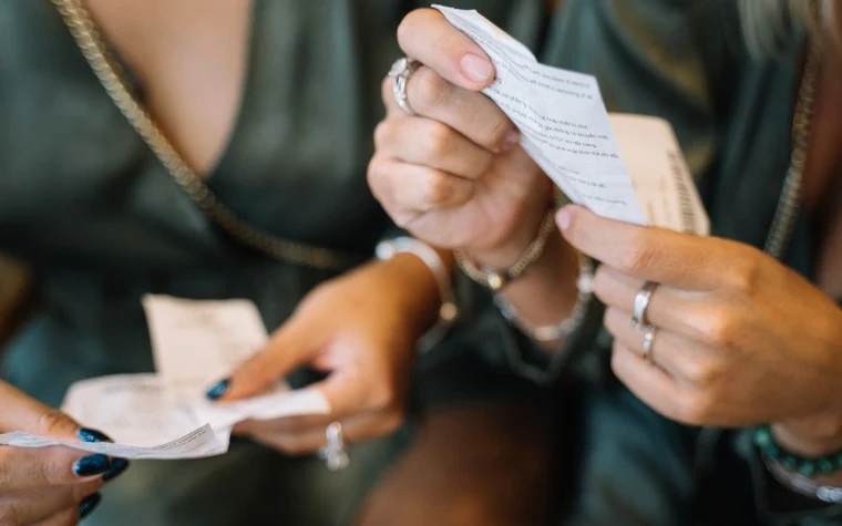 close-up of two pairs of hands holding and comparing small paper receipts and slips