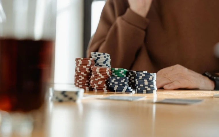 stacks of black and white poker chips and playing cards on a wooden table next to a glass of dark drink