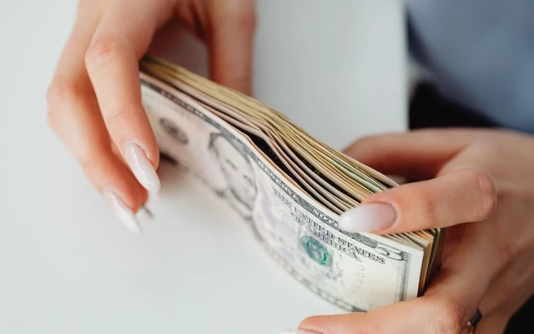 two hands holding a thick stack of US dollar bills