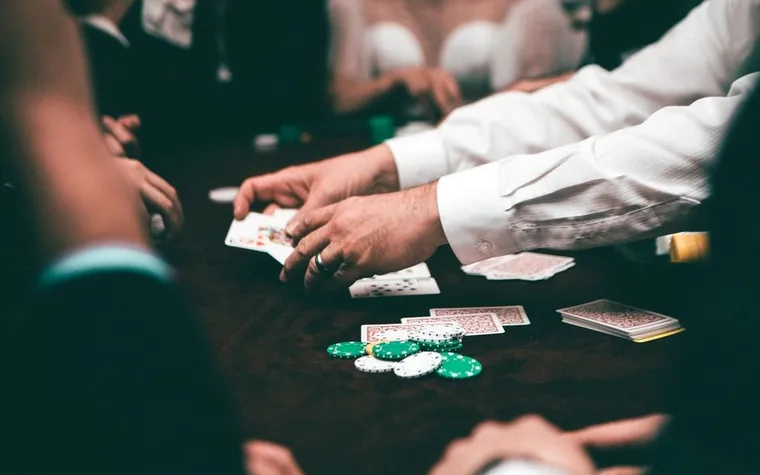 dealer and players with poker chips and cards spread on a dark casino table