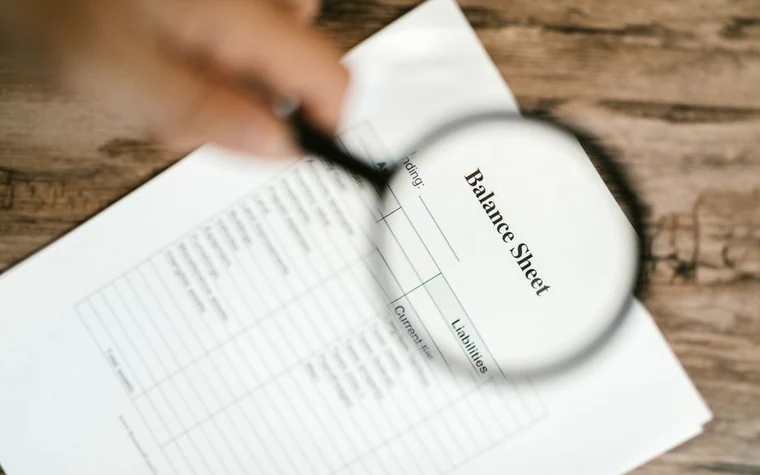 magnifying glass held over a printed balance sheet on a white desk