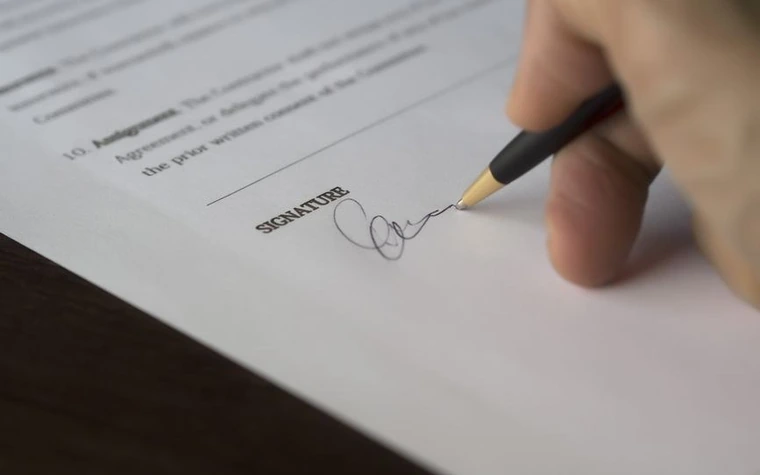 close-up of a hand signing a printed agreement with a pen
