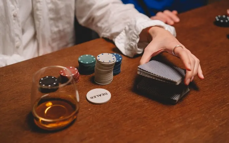 poker chips, cards and a dealer button on a wooden card table beside a glass