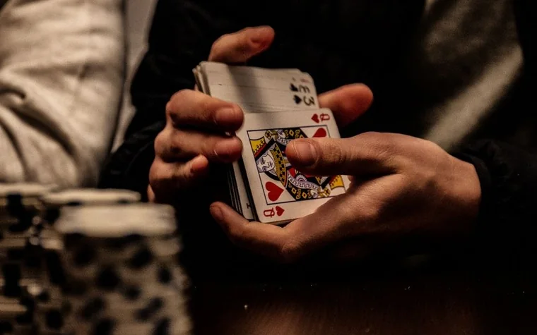 hands squaring a deck of playing cards beside stacked black chips on a dark table