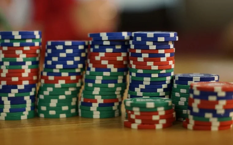 Stacks of red, blue and green poker chips of uneven height on a wooden table