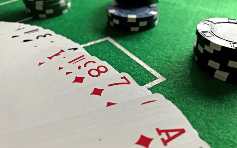 Fanned playing cards including the ace of diamonds beside black and blue chips on green felt