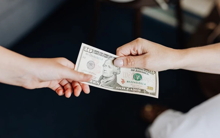 Two hands exchanging a folded US dollar bill as a tip