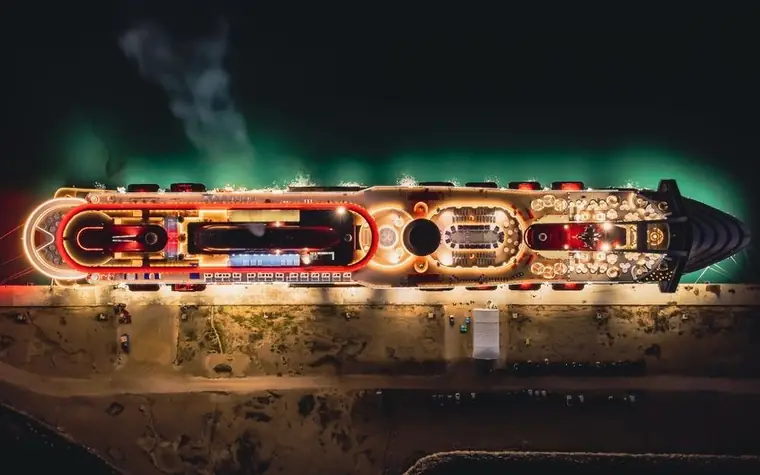 aerial night view of a large cruise ship docked in port, decks lit with colorful lights along the hull