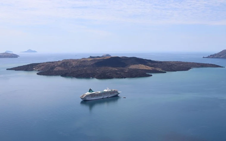 large white cruise ship anchored near a dark volcanic island coastline with calm blue water