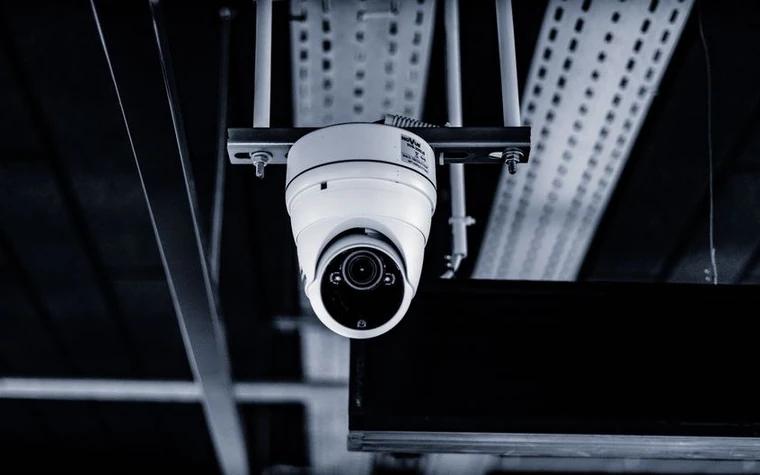 white dome security camera mounted on ceiling scaffolding, lit in a moody blue tone