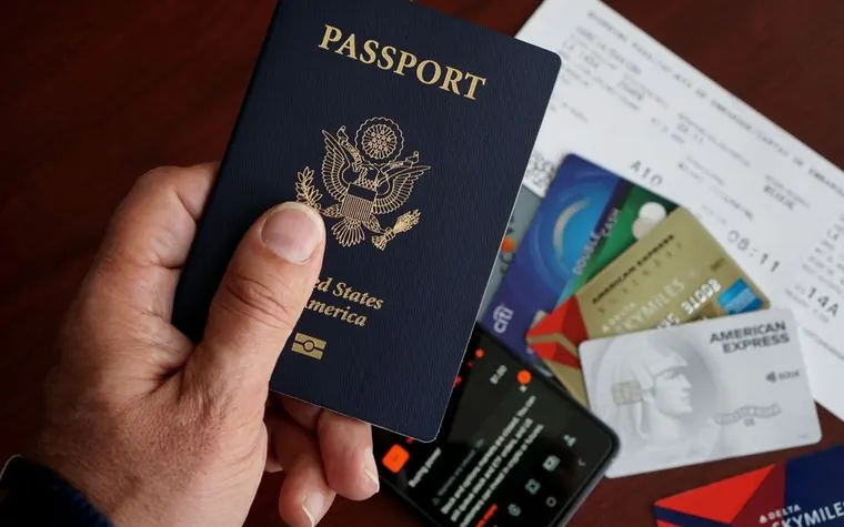 hand holding a US passport over a table with credit cards, a boarding pass, and a phone