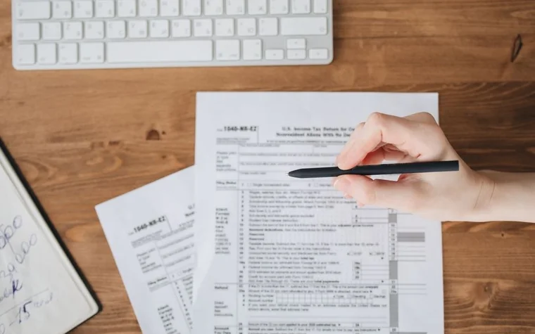 hand holding a pen over a 1040-NR-EZ nonresident tax form next to a keyboard