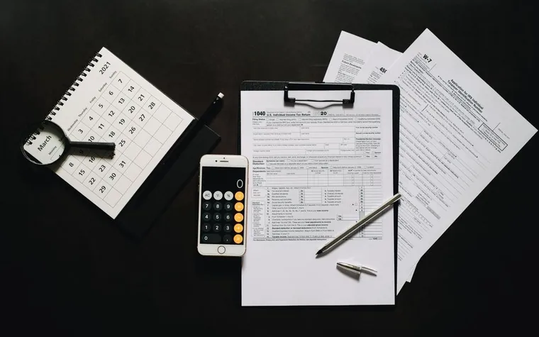 W-7 and 1040 tax forms on a clipboard next to a calculator, pen, and desk calendar