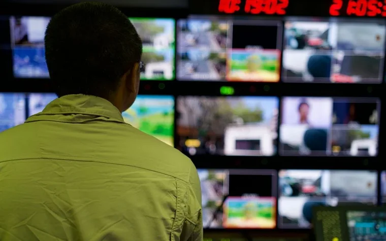 surveillance operator viewed from behind, watching a wall of camera feed monitors in a casino control room