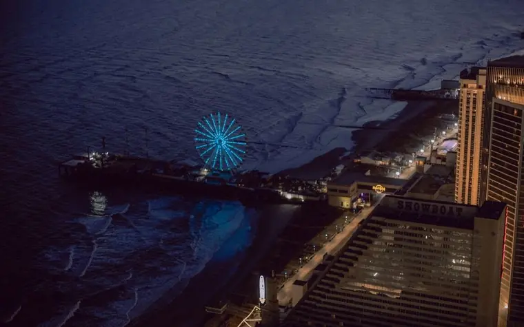 Aerial night view of Atlantic City boardwalk with illuminated ferris wheel, beach and hotel towers
