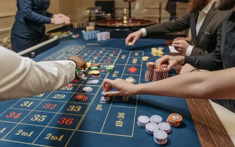 Players placing chip bets on a blue felt roulette table as a dealer looks on