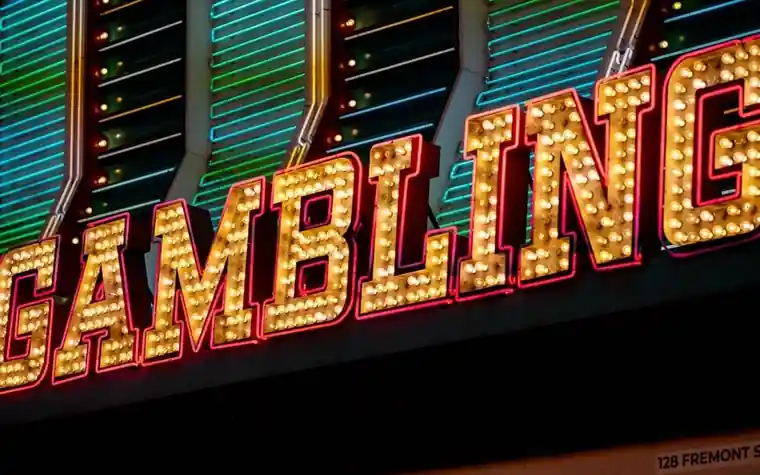 Vintage marquee sign spelling GAMBLING in yellow bulb letters against striped neon light panels