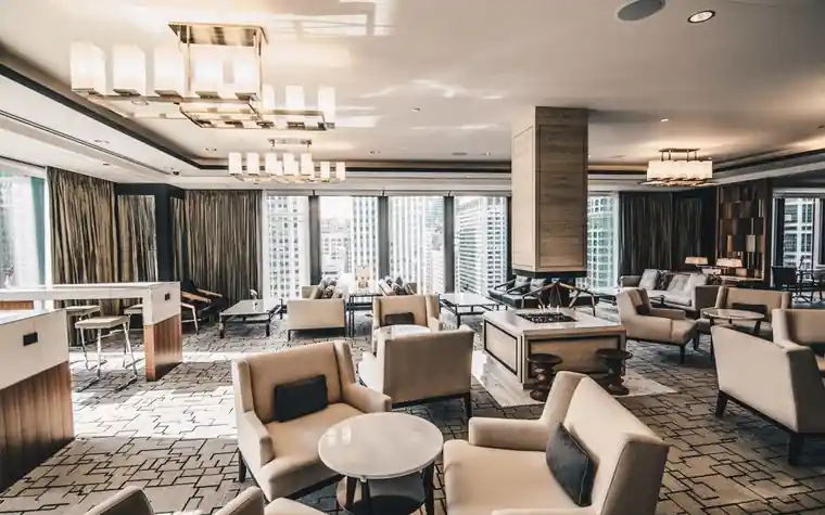 Spacious hotel lounge with cream armchairs, low tables and tall windows, with no guests in the frame