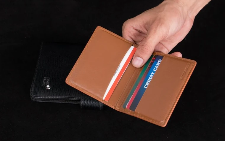 Hand holding open a brown leather wallet with several plastic cards tucked into its slots