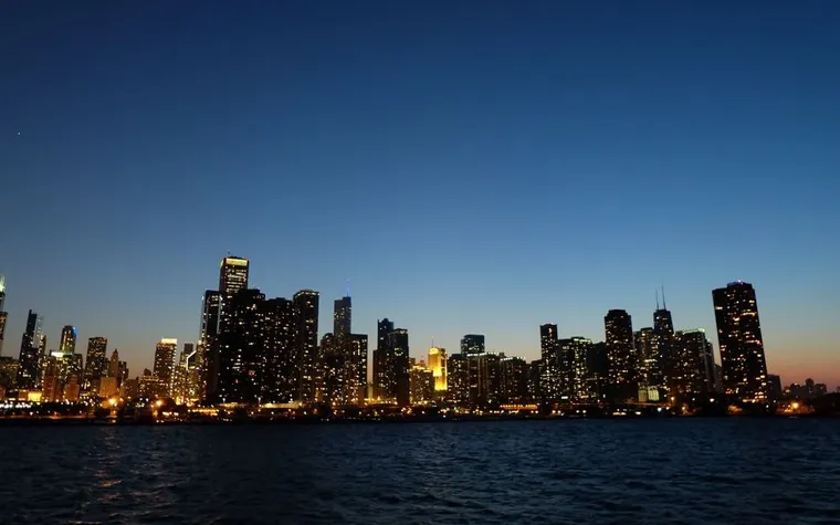 Chicago skyline at dusk with lit towers reflected in the dark water of Lake Michigan