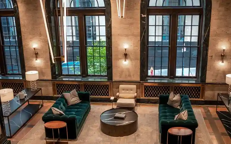 Spacious hotel lobby with green velvet sofas, wall sconces and tall arched windows with no guests in view