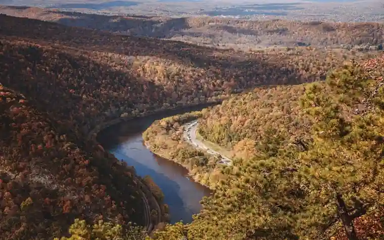winding river between forested hills dressed in orange and green autumn foliage seen from a high overlook