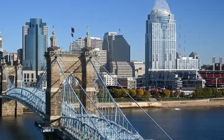 Cincinnati skyline with tall glass office towers behind the blue steel cables of the Roebling suspension bridge on the river