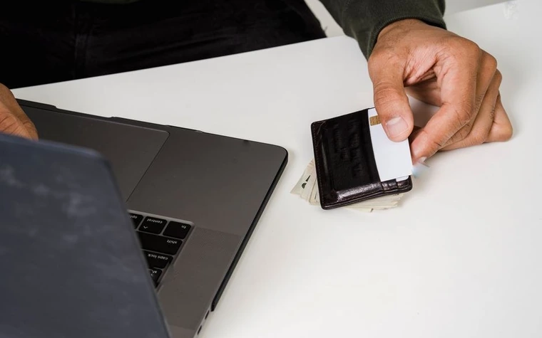 man's hand sliding a white plastic card into a black card holder beside an open laptop on a white desk