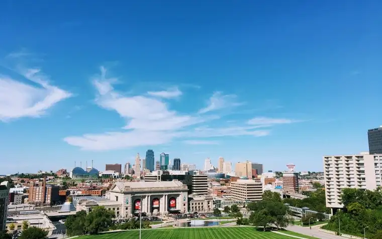 wide view of the Kansas City skyline and a stone train station building beneath a bright blue sky with scattered clouds