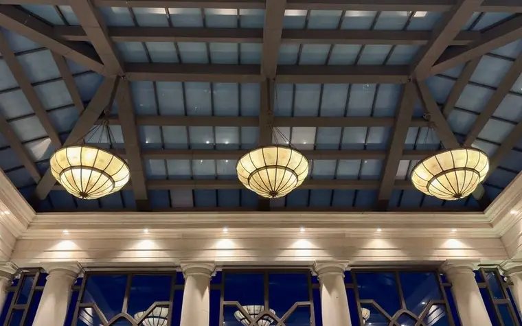 hotel lobby seen from below with a glass-paneled ceiling, white columns and three large round glowing light fixtures