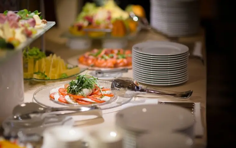 buffet table with plated tomato and mozzarella salads, fruit platters and a stack of white plates