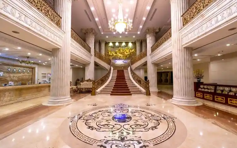 Hotel foyer with a marble floor, tall columns and a grand carpeted staircase under a chandelier